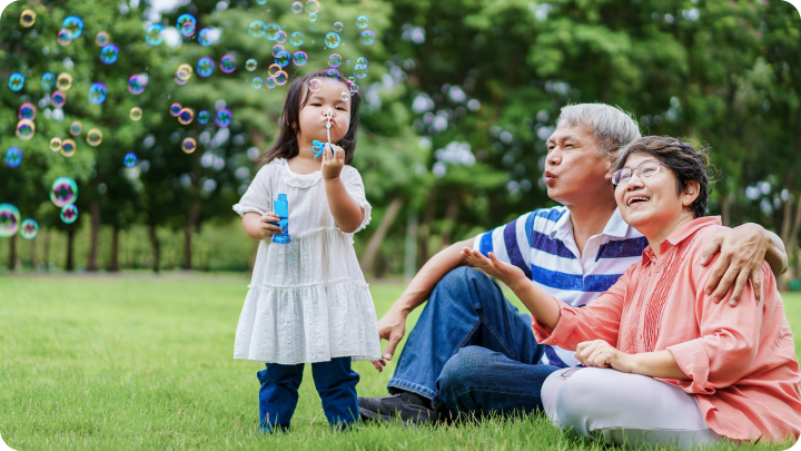 grandparents with grandchild blowing bubbles in a field